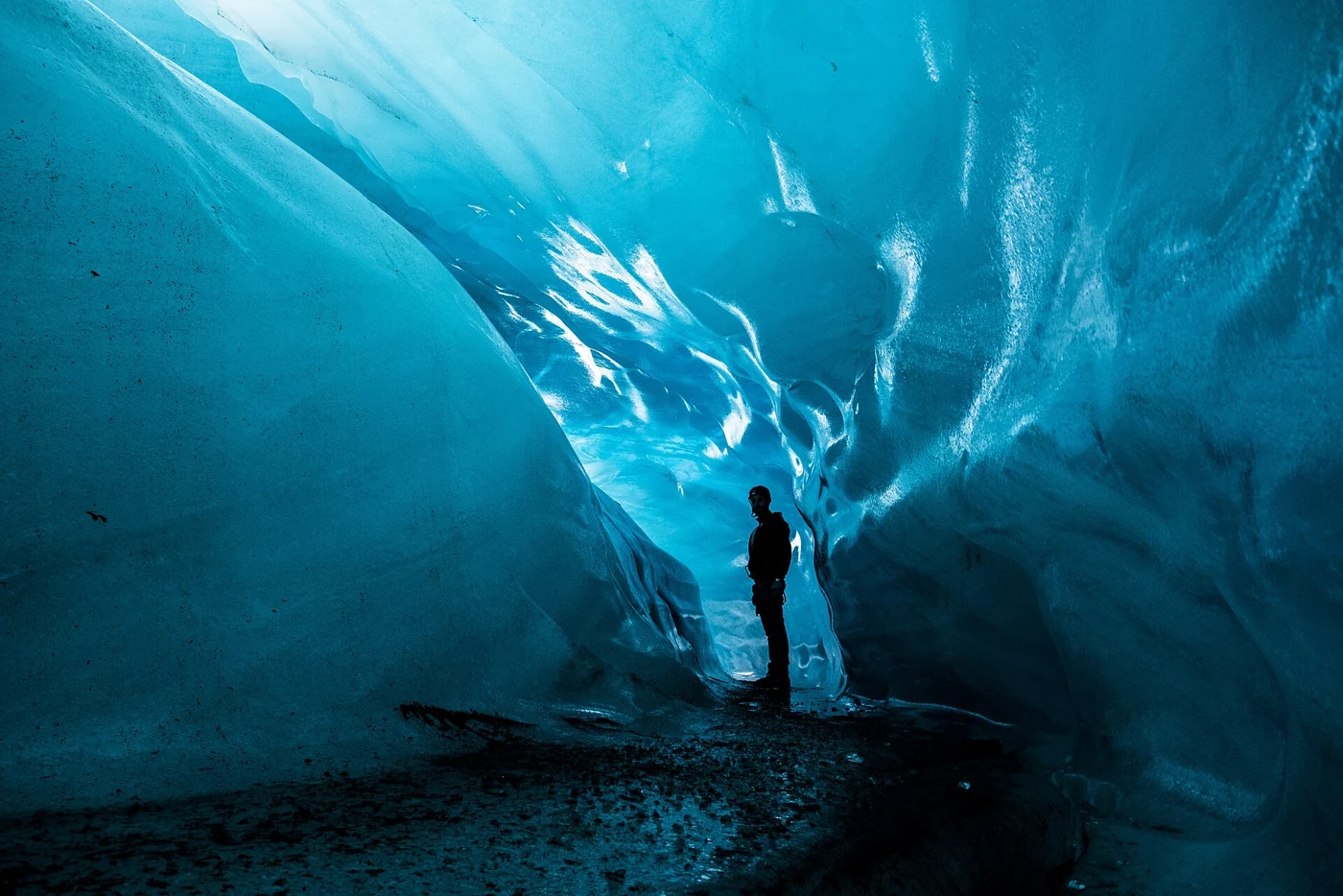 A lone figure dwarfed by curving blue ice walls in an ice cave in Vatnajökull National Park, reached on an Iceland ice cave day tour